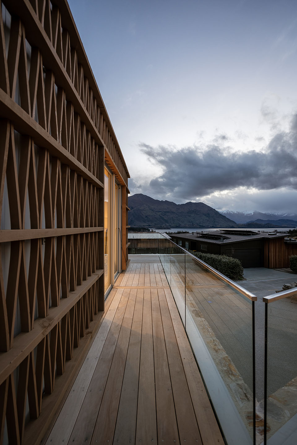 Akitu IV upper deck with a glass balustrade and curved timber rainscreen framing views toward Lake Wānaka and the mountains.