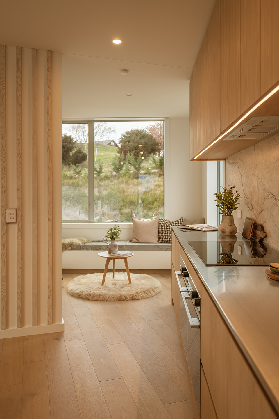Akitu IV kitchen beside a built-in window seat, with timber cabinetry and a large window overlooking the planted hillside.