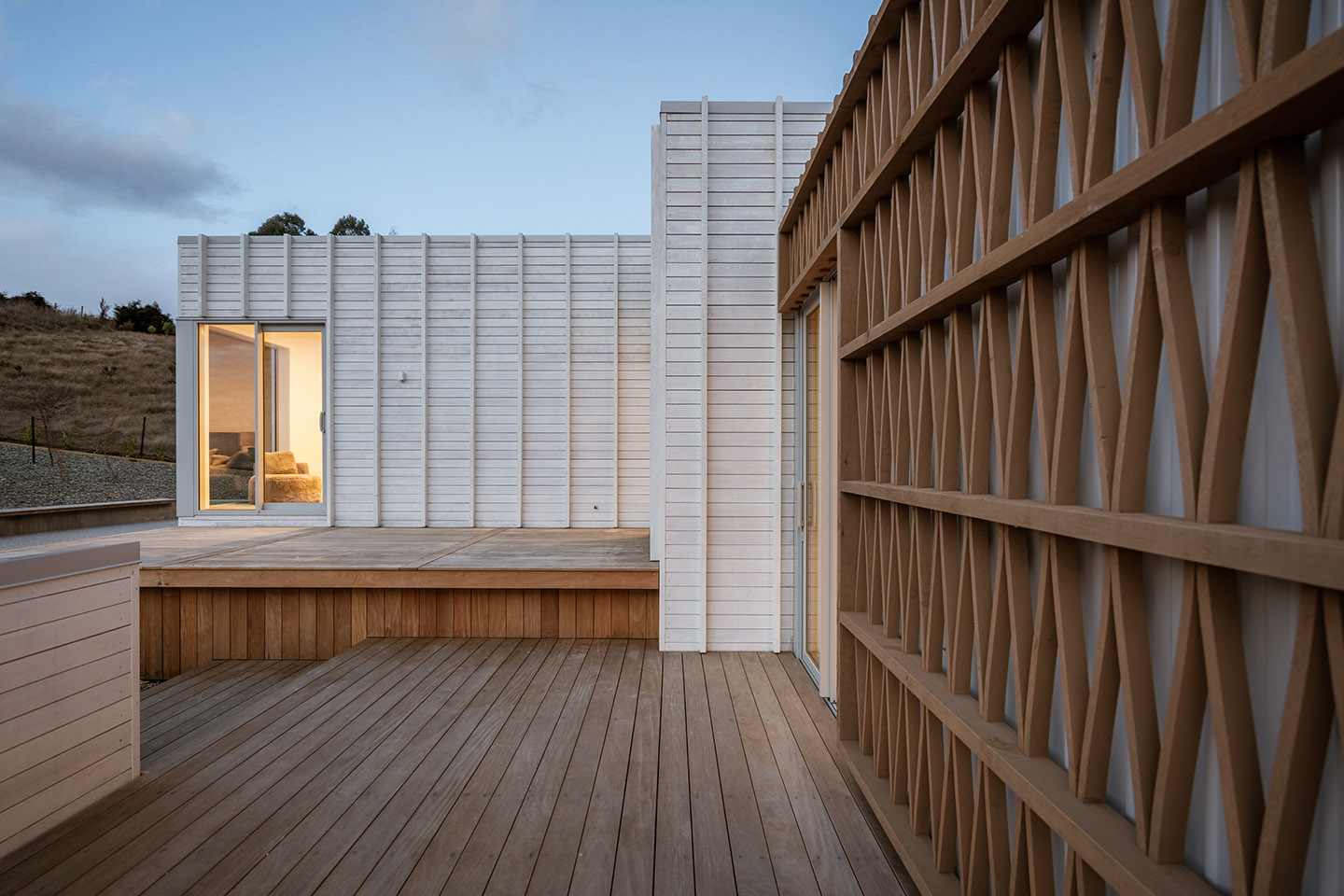 Akitu IV courtyard deck at dusk with pale clad walls and the curved timber rainscreen extending along the glazed elevation.