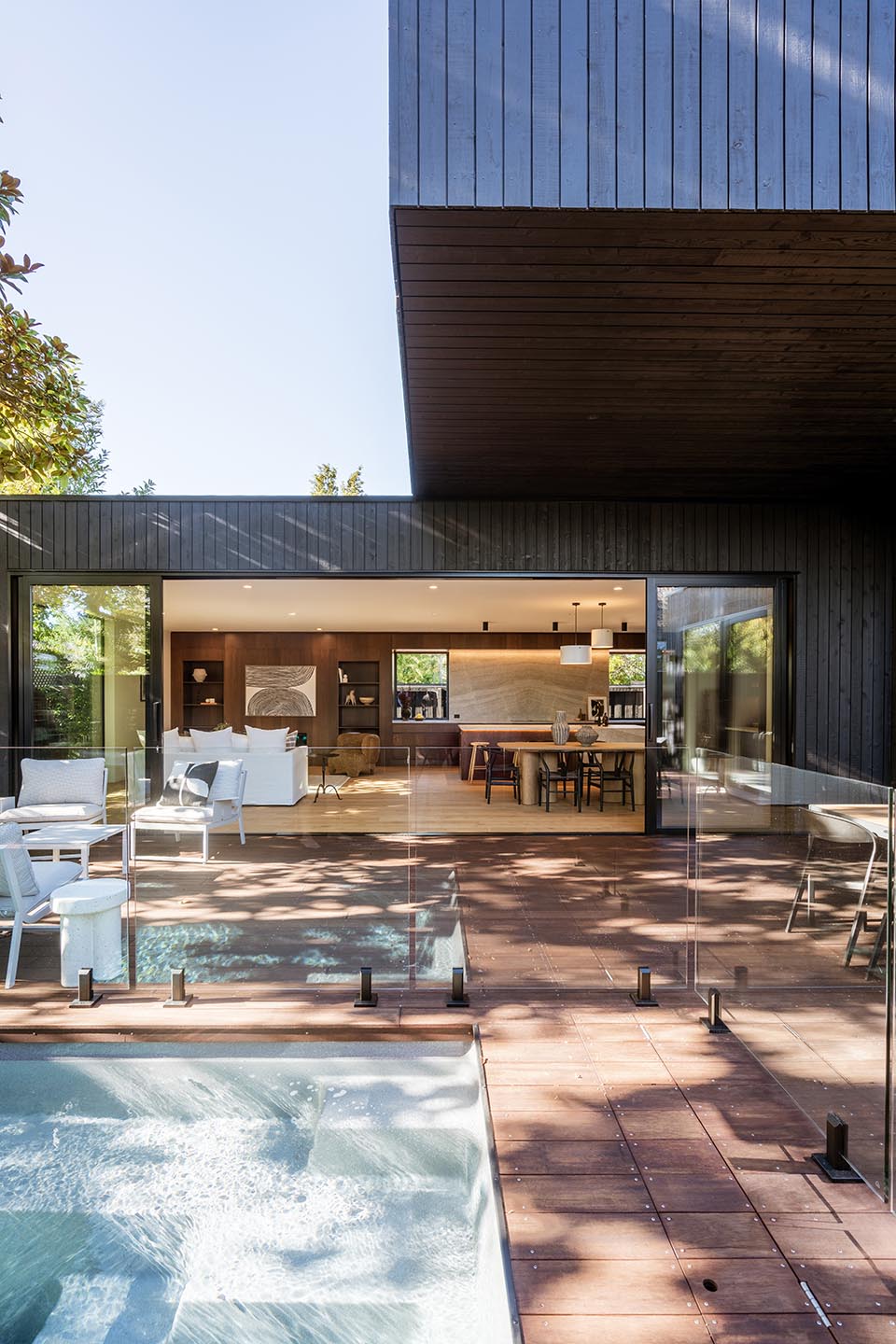 Bryndwr I pool courtyard with dark vertical timber cladding, deep upper-level cantilever and wide glazing opening the living area to the deck.
