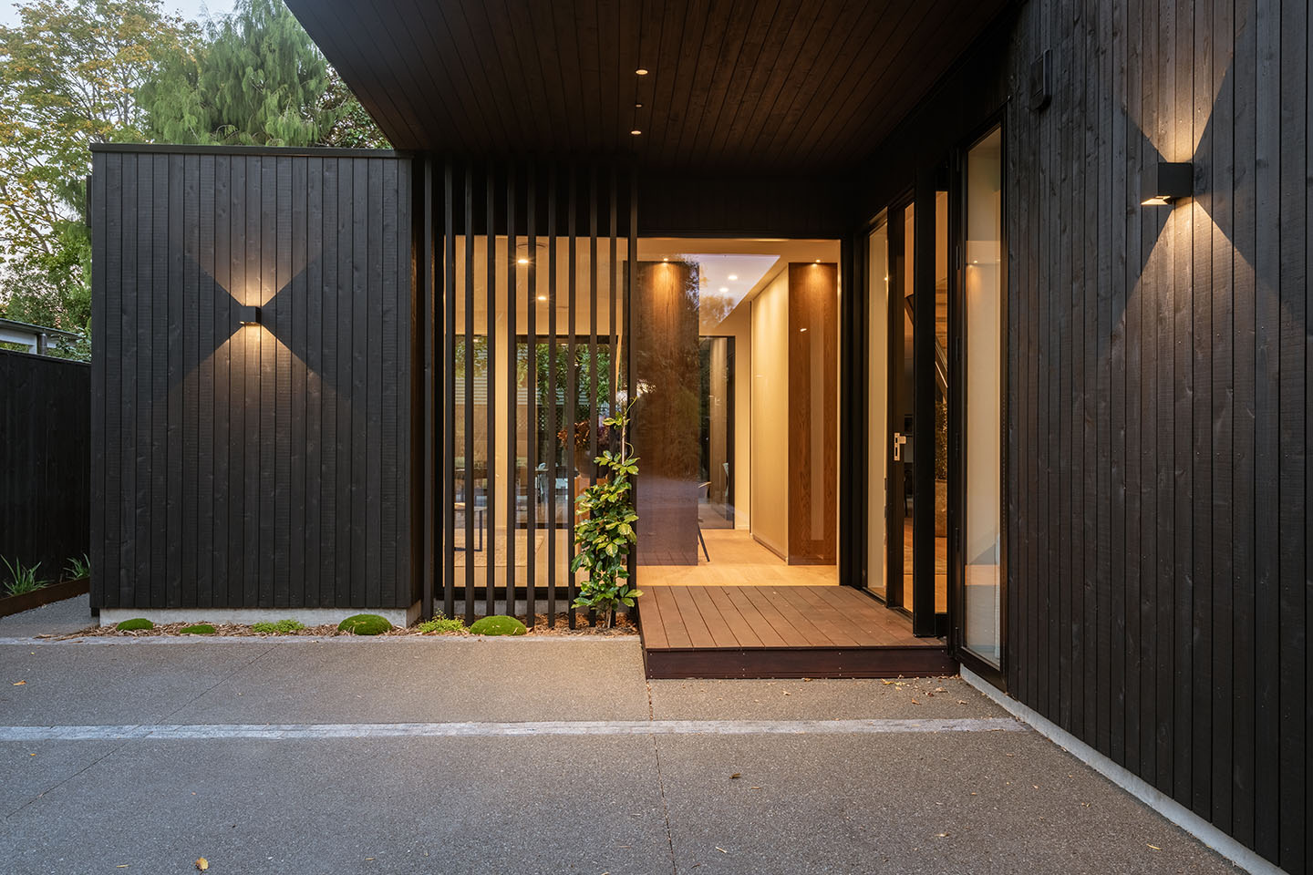 Bryndwr I entrance with vertical timber screening, dark cladding and a sheltered timber-lined approach beneath the upper level.