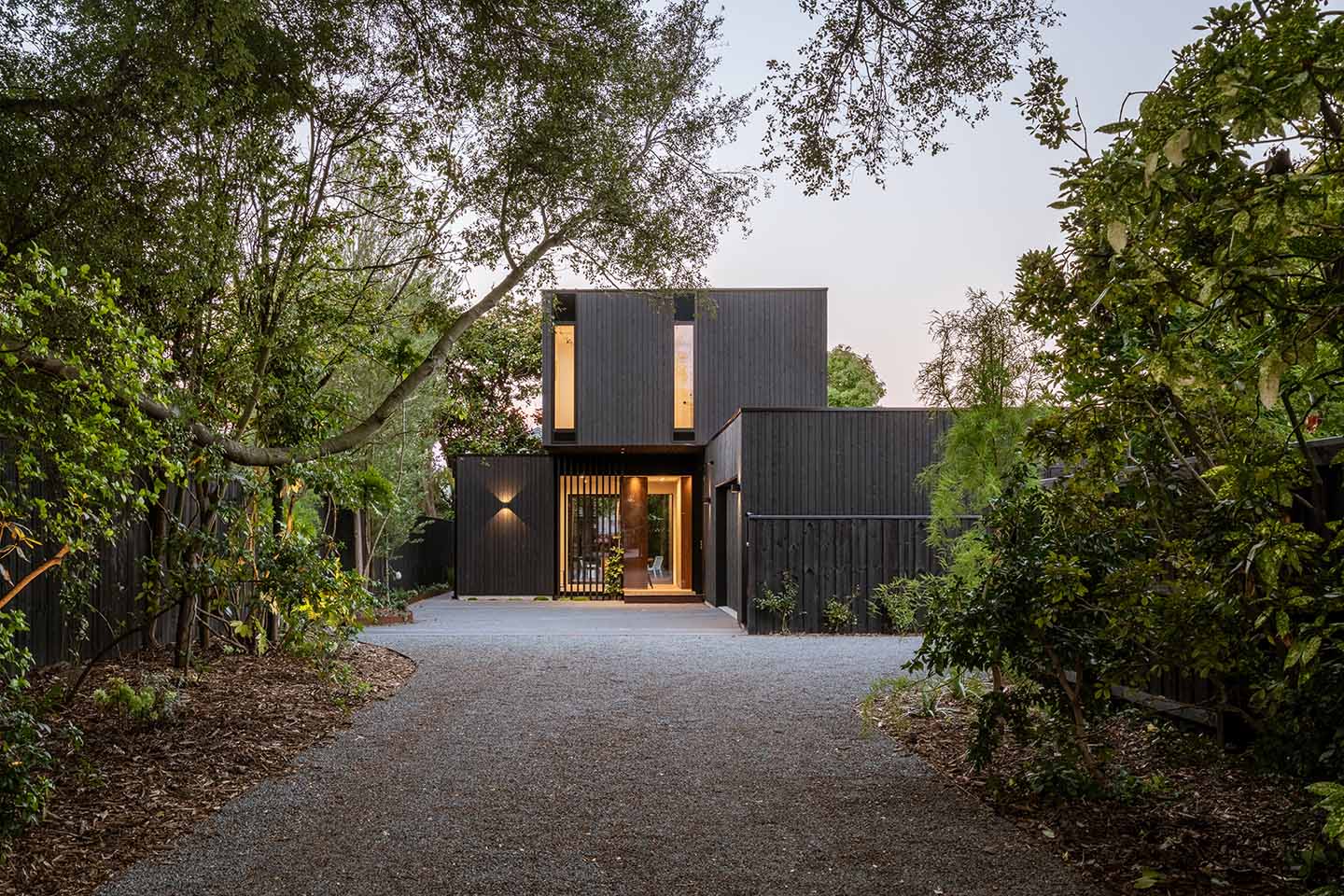 Bryndwr I viewed along the mature tree-lined driveway, with dark timber-clad forms framing the recessed entrance.