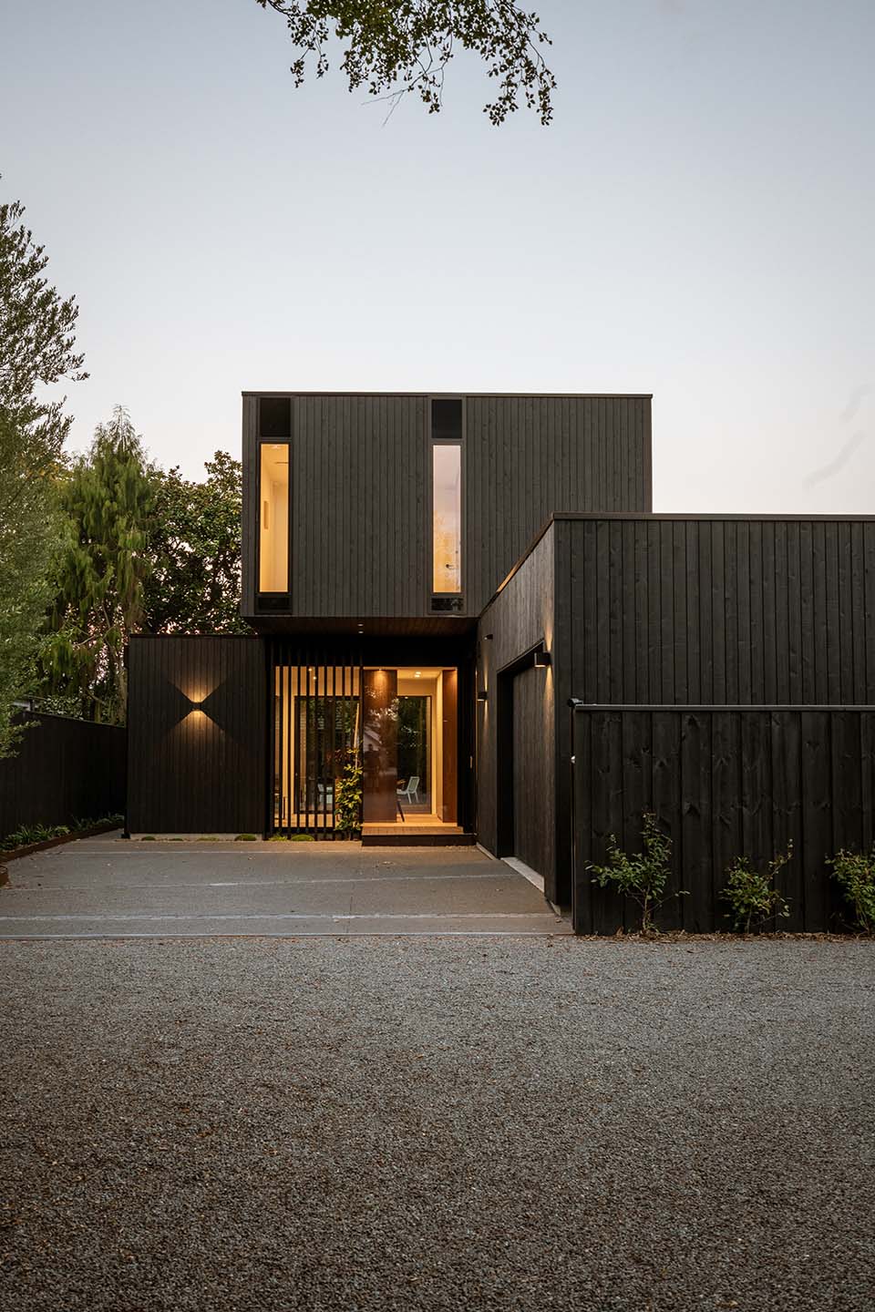 Bryndwr I front elevation at dusk with dark vertical timber cladding, narrow upper-level windows and a screened entrance below.