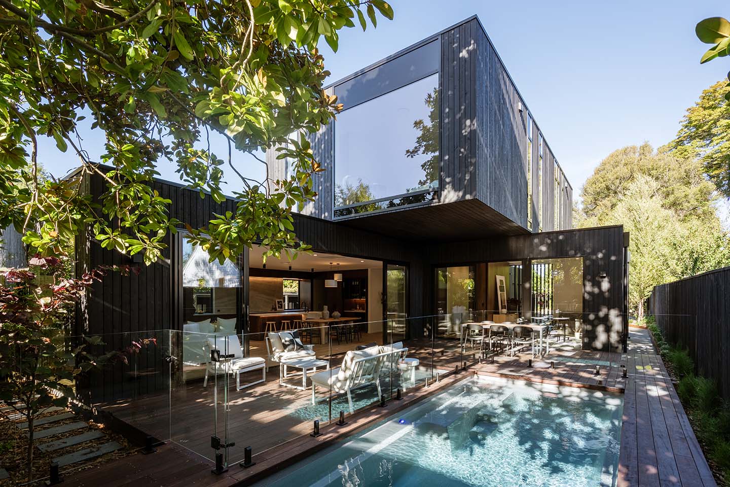 Bryndwr I rear exterior with dark timber cladding, a deep cantilevered upper level and full-height glazing around the pool courtyard.
