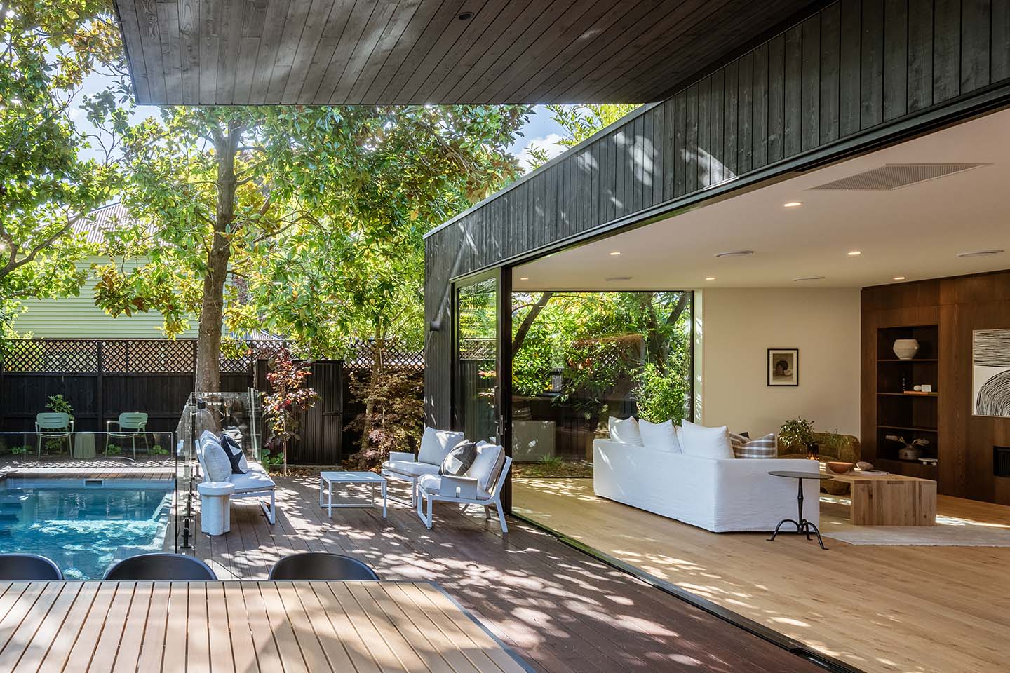Bryndwr I living room opening through full-height sliding glazing to the timber deck and pool beneath a dark timber soffit.