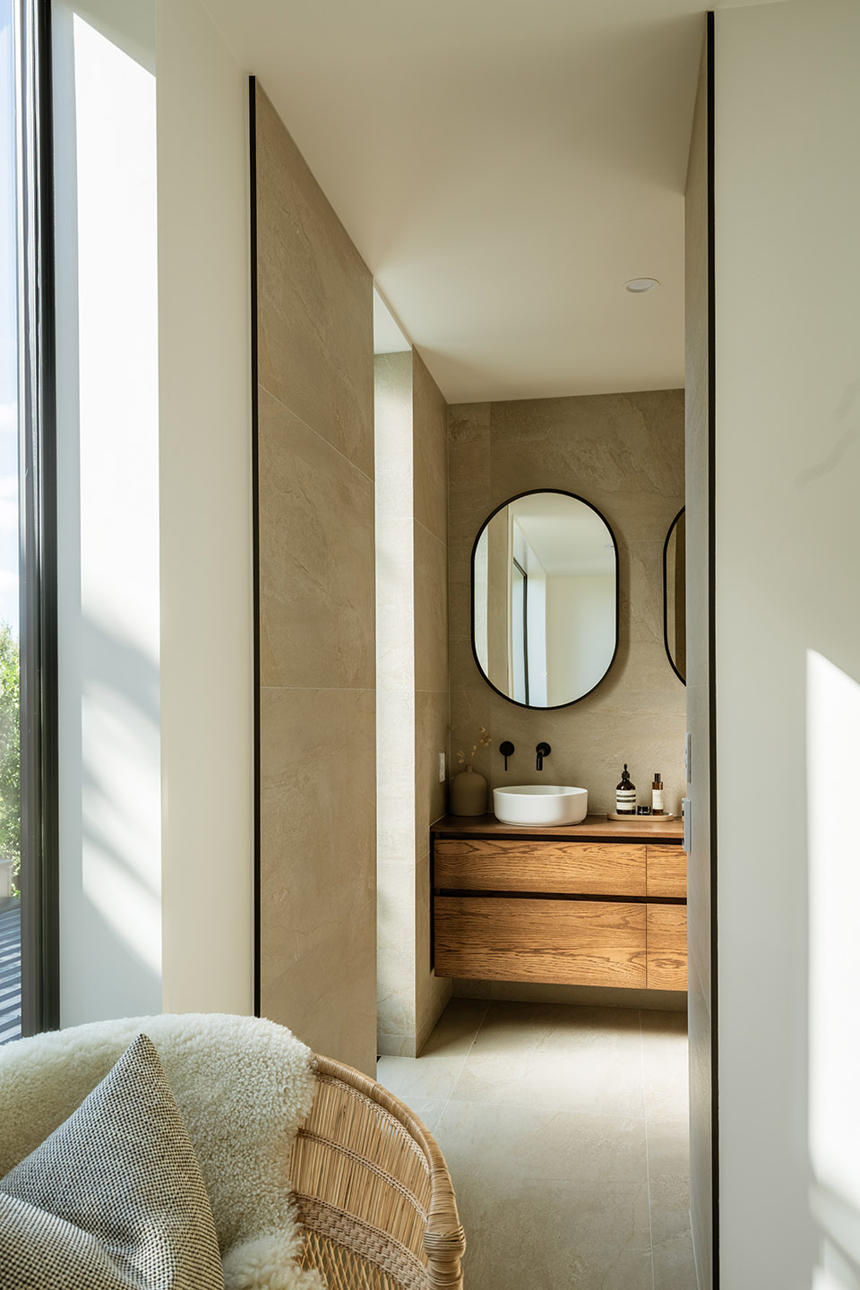 Bryndwr I ensuite with timber vanity, round mirror and pale tiled walls beside the bedroom seating area.
