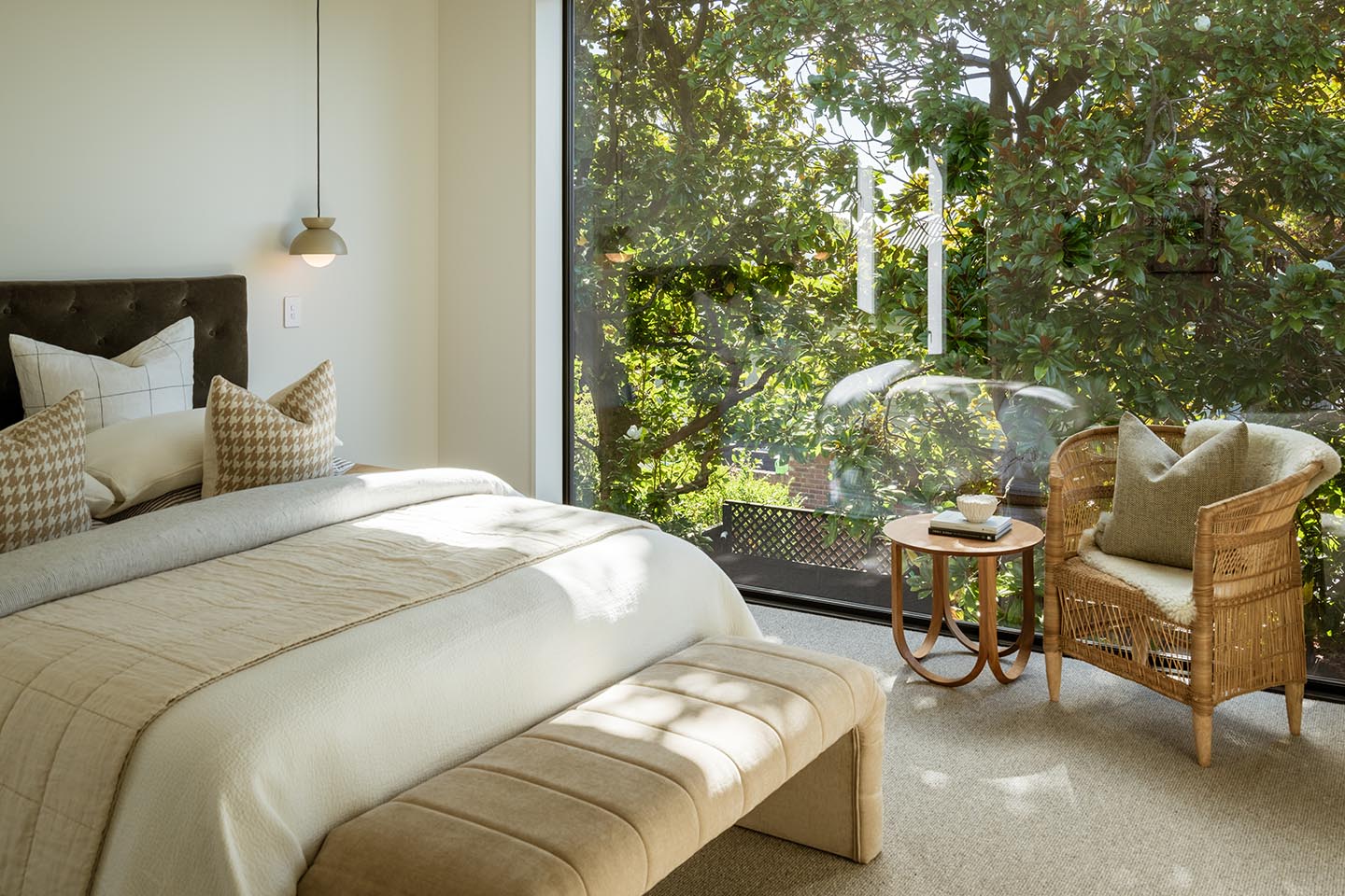 Bryndwr I bedroom with full-height glazing looking into mature trees, with a sitting chair positioned beside the window.