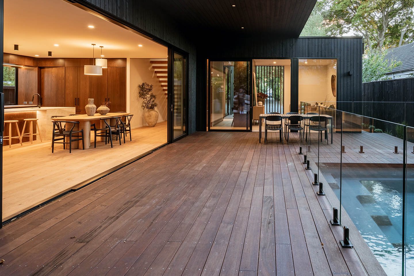 Bryndwr I pool deck at dusk with large sliding openings connecting the kitchen, dining and living spaces to the courtyard.