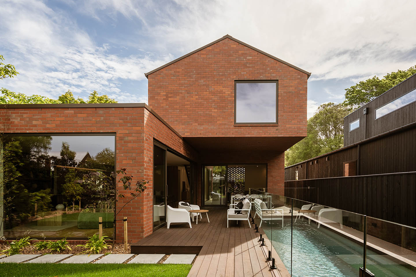 Bryndwr II rear elevation with a cantilevered brick upper level, sheltered timber deck and narrow swimming pool.