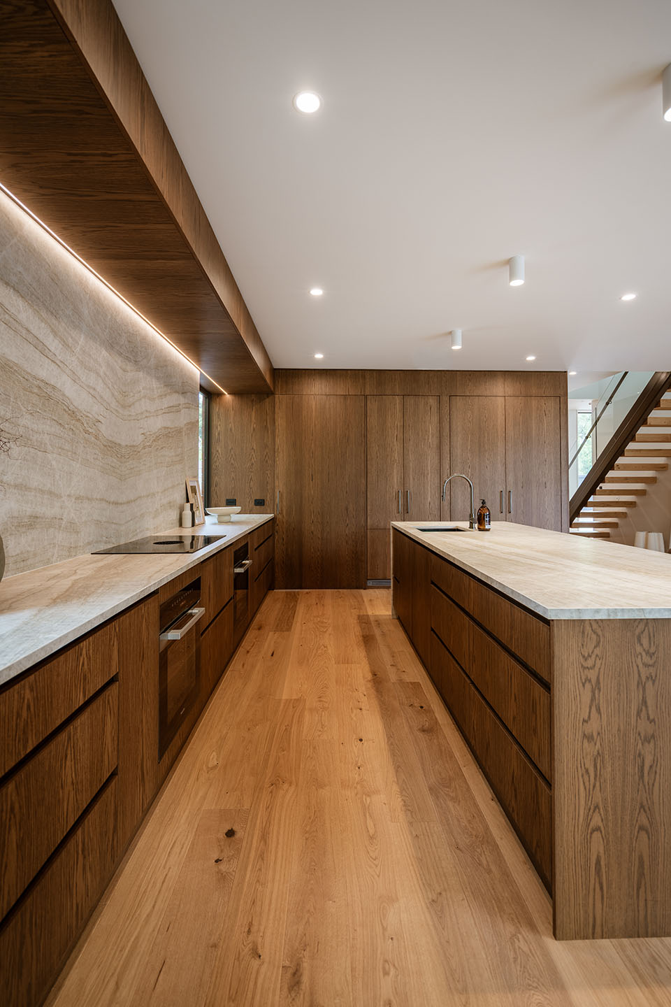 Bryndwr II kitchen with dark timber cabinetry, pale stone benchtops and timber flooring beside the open stair.