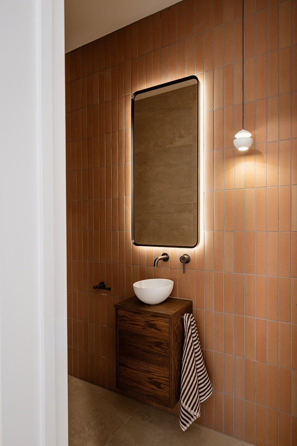 Bryndwr II powder room with terracotta-toned wall tiles, timber vanity, vessel basin and illuminated mirror.