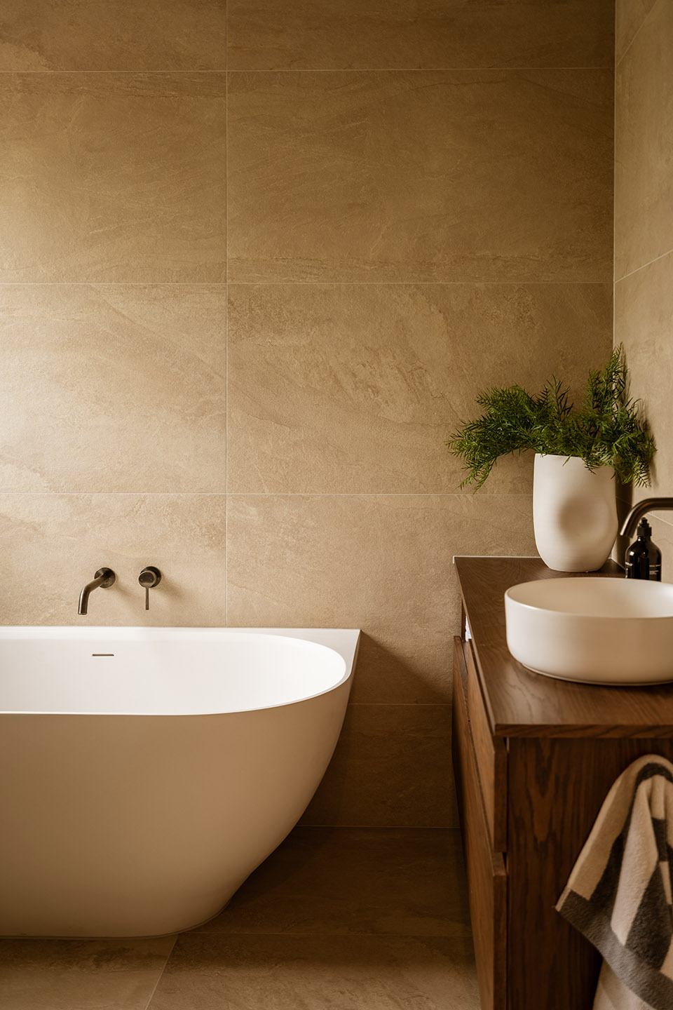 Bryndwr II bathroom with freestanding bath, timber vanity and warm neutral tiles across the walls and floor.