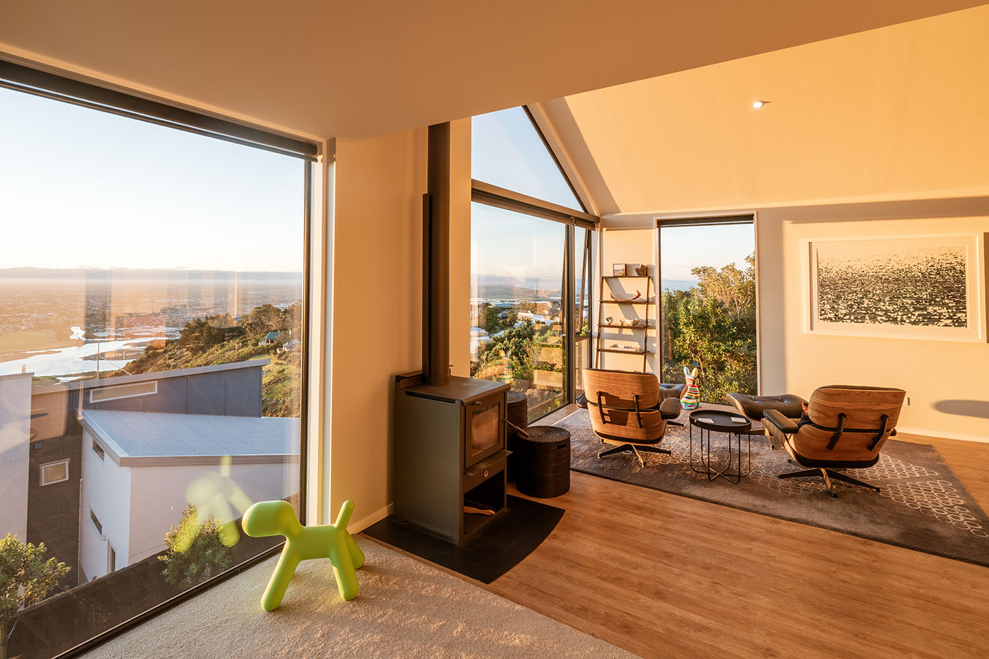 Major Hornbrook II sitting area with a freestanding fireplace and tall corner glazing overlooking Christchurch, the estuary and distant coast.