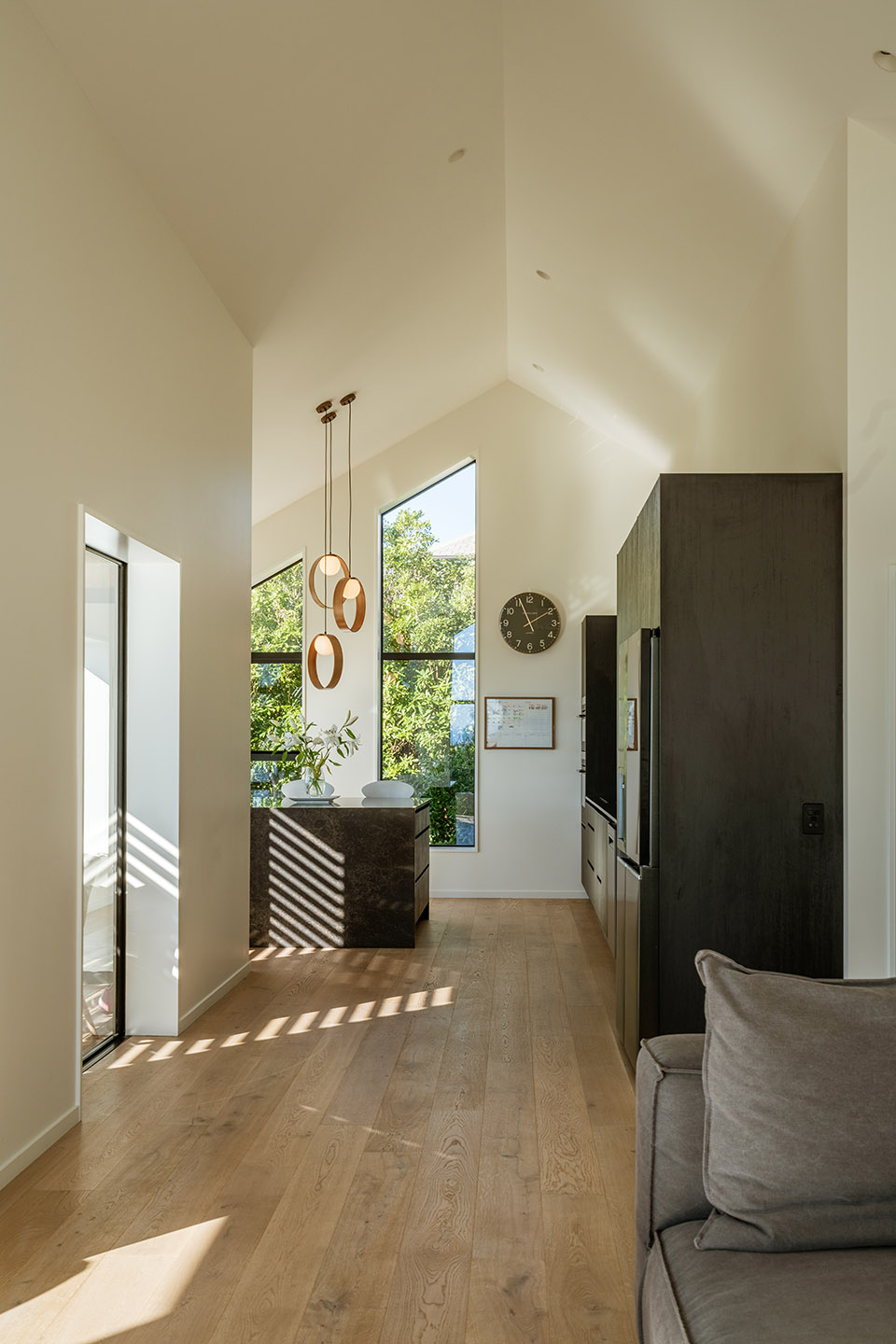 Revelation III kitchen and living area with timber flooring, dark cabinetry, high ceilings and tall glazing bringing light into the interior.