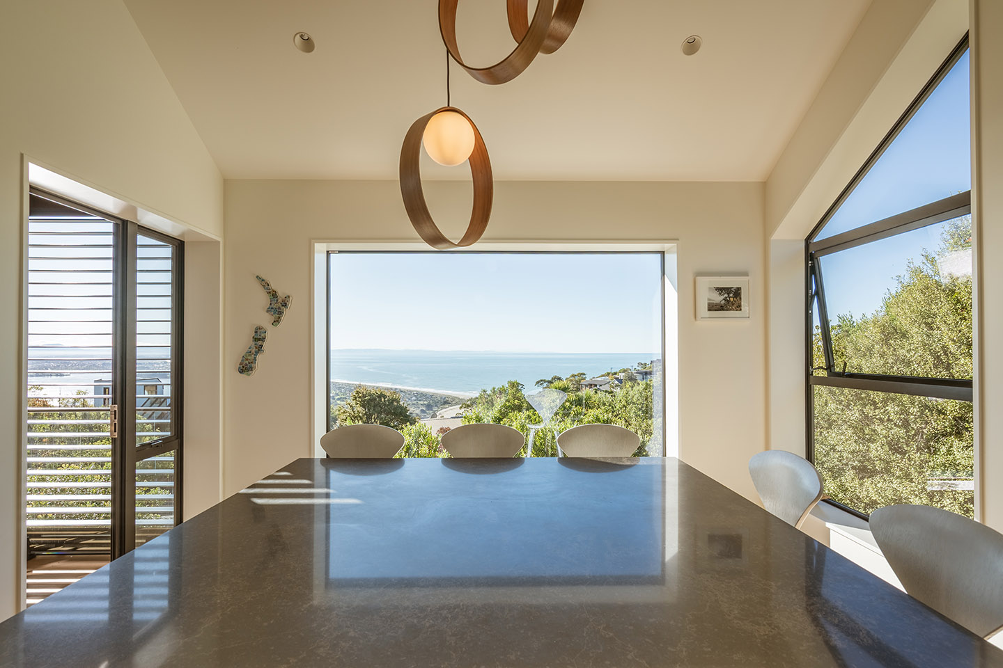 Revelation III dining area with a dark table, sculptural pendant lights and large windows framing expansive coastal views.