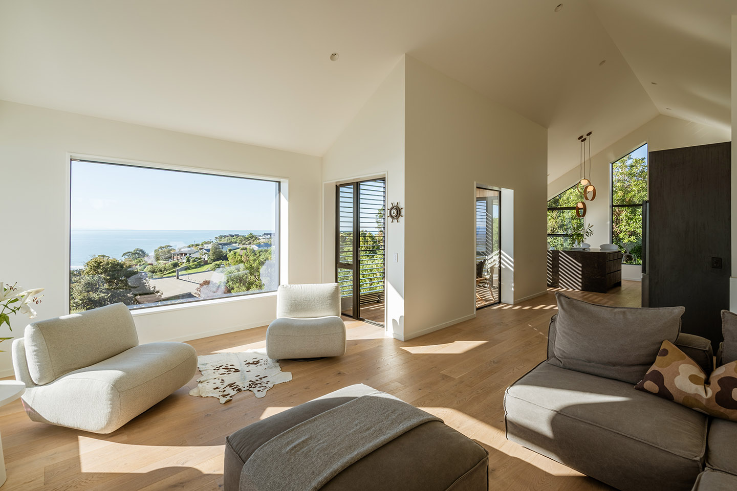 Revelation III living area with timber flooring, soft seating and large windows framing elevated coastal views.