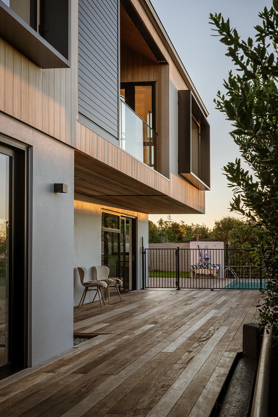 Revelation III exterior at dusk with a projecting timber-clad upper level, glazed balcony and broad timber deck beside the pool.